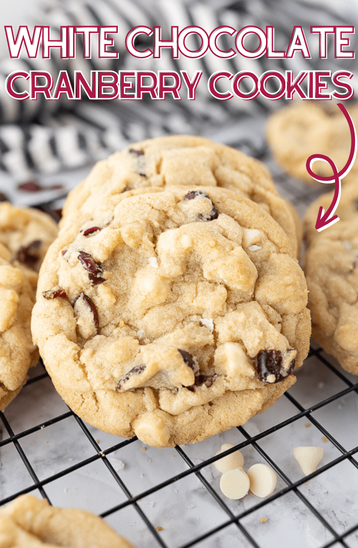 A cranberry white chocolate chip cookie on a cooling rack with red and white writing on the photo that reads "White chocolate cranberry cookie."