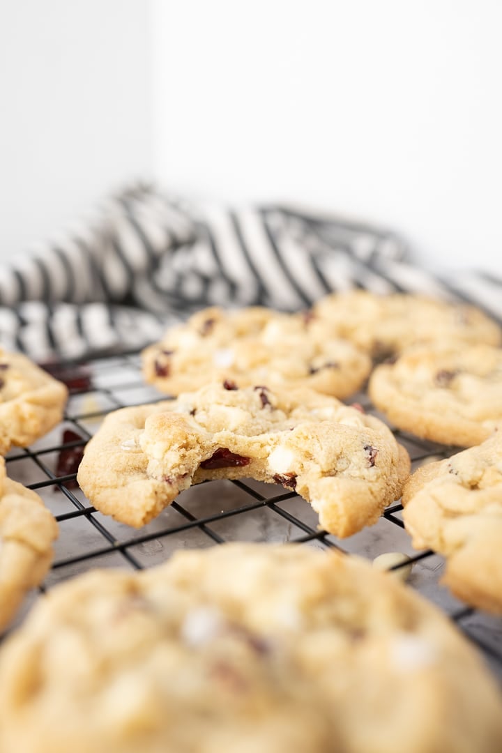 White chocolate cranberry cookies on a cooling rack with a bite taken out of one cookie.