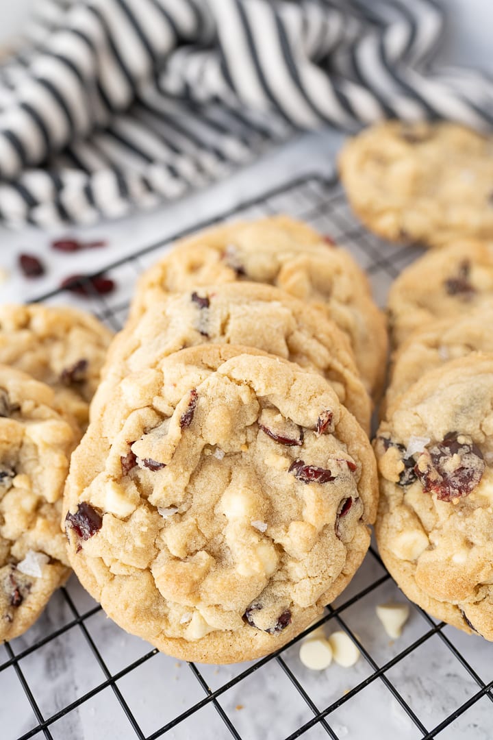 White chocolate cranberry cookies laying on a cooling rack with a black and white striped towel in the background.