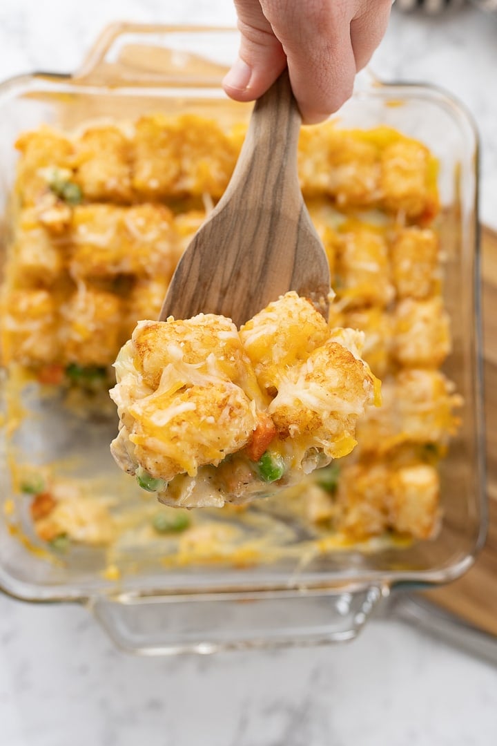 A hand with a spatula serving up a slice of chicken tater tot casserole.