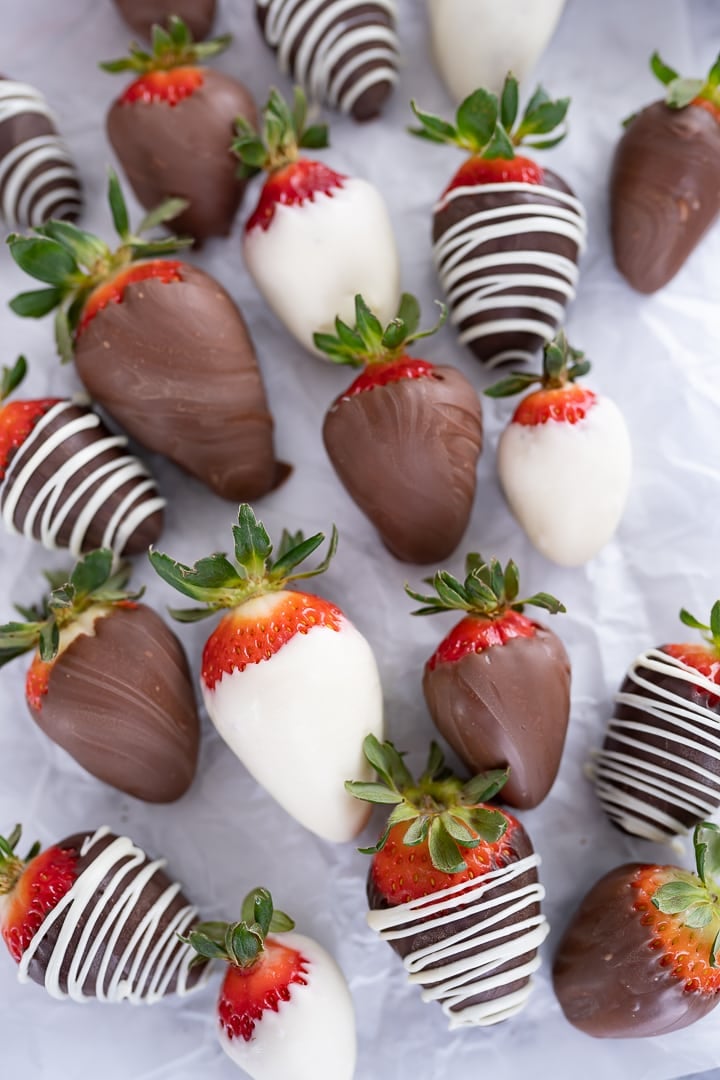 Several strawberries on the counter, dipped in white and milk chocolate.