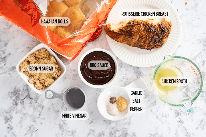 Ingredients on the counter in small dishes including hawaiian rolls, rotisserie chicken, brown sugar, bbq sauce, white vinegar, garlic, salt, pepper, and chicken stock.