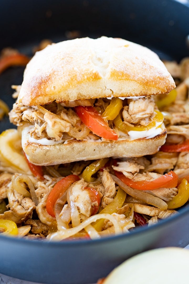 A chicken philly sandwich stacked on top of cheesy chicken and veggies in a pan.