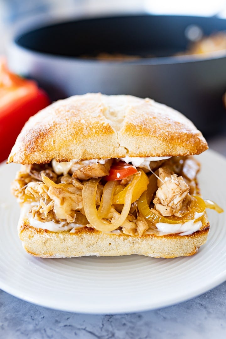 A chicken philly cheesesteak on a plate with a pan in the background.