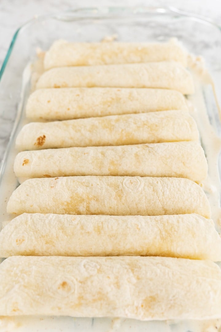 Filled and rolled up tortillas in a baking pan on the counter, without any toppings.