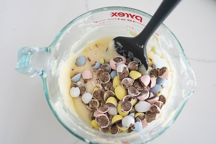 Cadbury eggs mixed with melted white chocolate in a glass bowl on the counter.