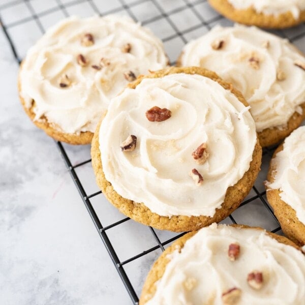 Carrot Cake Oatmeal cookies on a cooling rack topped with cream cheese frosting and chopped pecans.