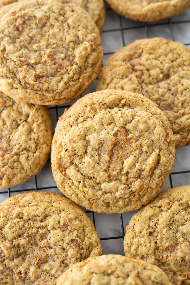 Several unfrosted carrot cake oatmeal cookies on a cooling rack on the counter.