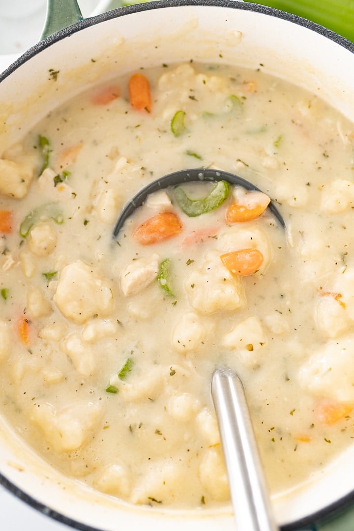 An overhead photo of chicken and dumplings soup in a pot with a ladle scooping some soup out.