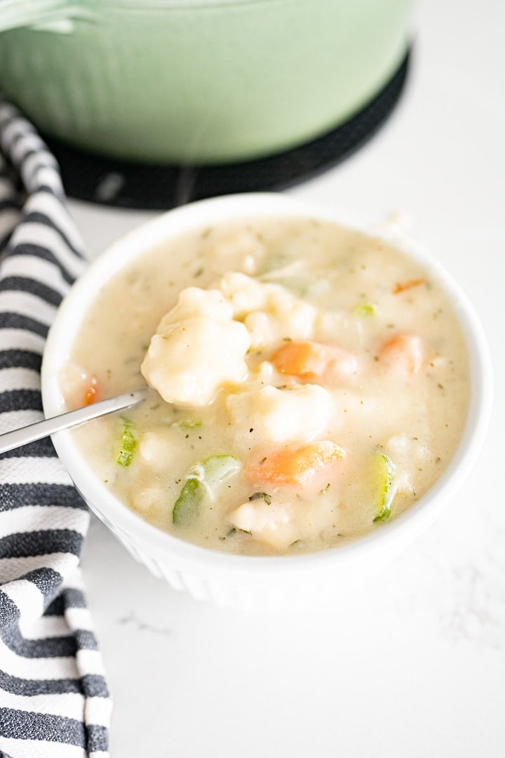 A white bowl on the counter filled with chicken and dumplings soup.