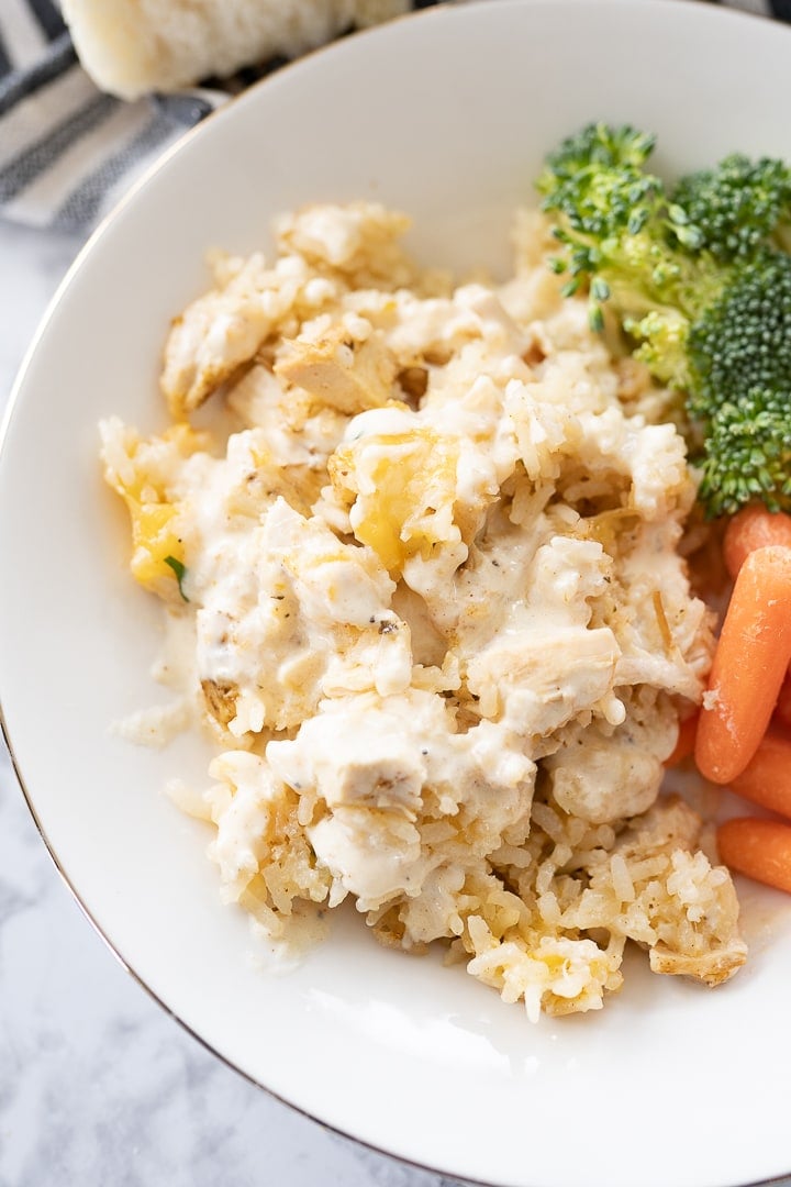 Cheesy chicken and rice casserole on a plate with carrots and broccoli.