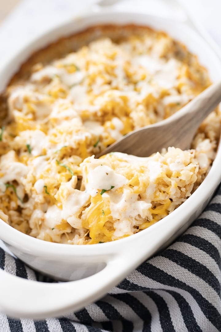 Chicken and Rice Bake in a white casserole dish on the counter with a wooden serving spoon scooping the casserole.
