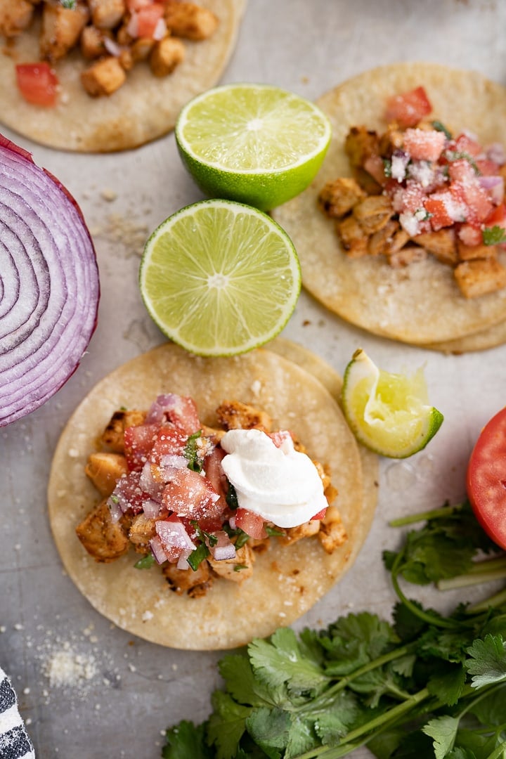 Tortillas topped with chicken, pico, sour cream, and other taco toppings on the counter.
