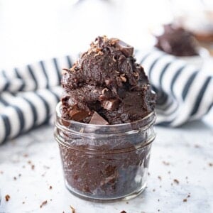 A glass jar overflowing with edible brownie batter stuffed with chocolate chunks.
