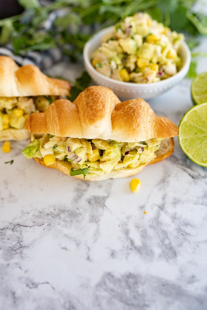 chicken salad sandwich with avocado in a croissant roll on the counter.