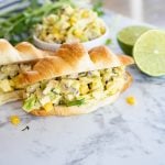avocado chicken salad on a croissant with avocado, chicken, corn, cilantro and lime on the counter.