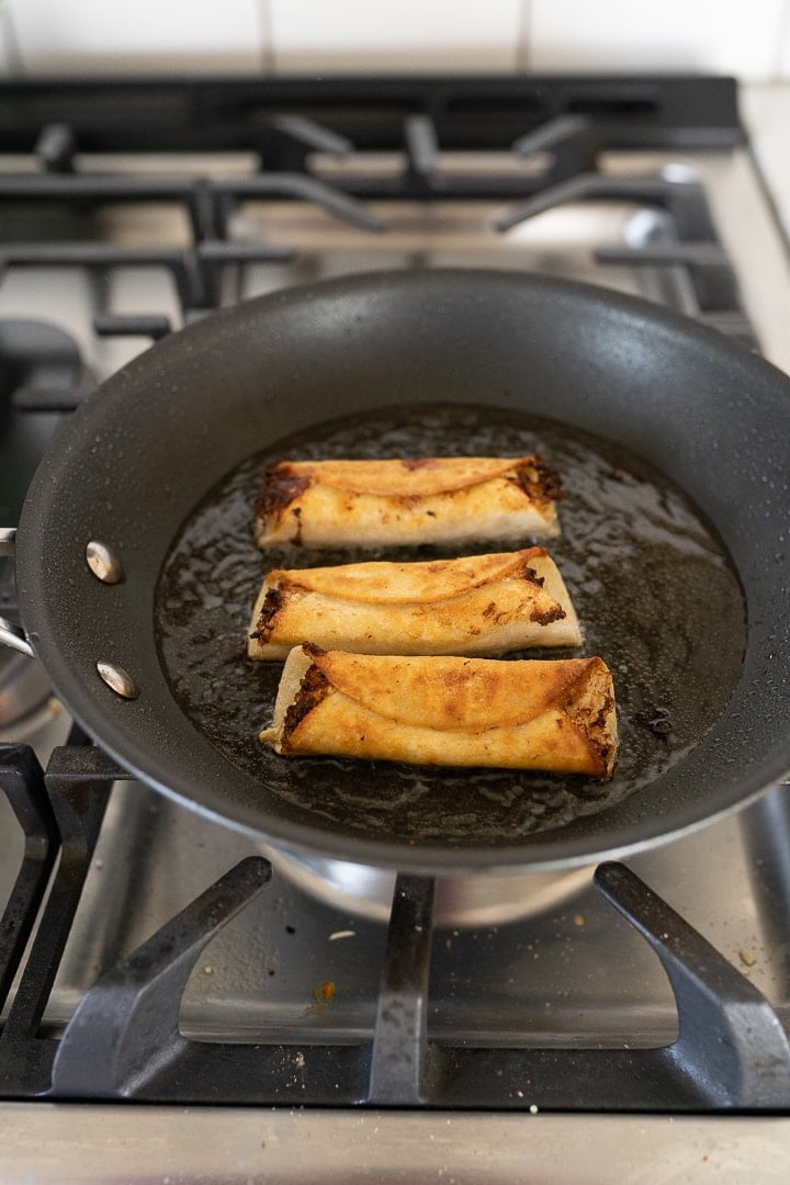 3 fried chicken taquitos in a pan on the stove. 