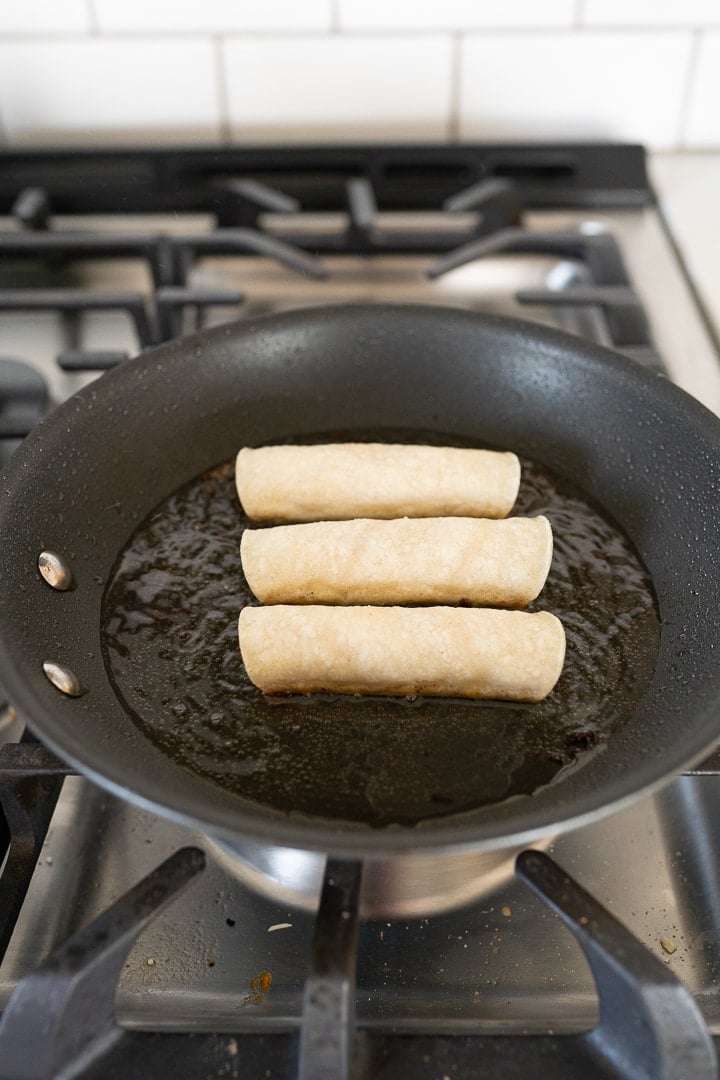 3 unfried chicken taquitos in a pan on the stove. 