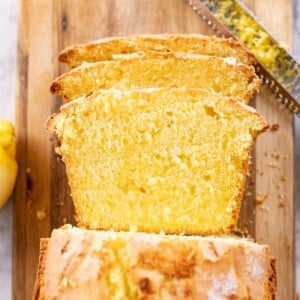 Bird's eye view of a lemon bread loaf on a wooden cutting board with slices stacked in front and a knife in the upper right hand corner.