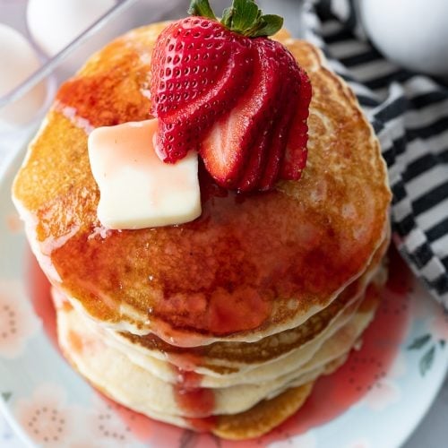 strawberry pancake syrup on a stack of pancakes with slices of strawberries on top.