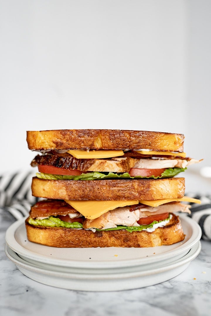 Side view of a double decker chicken club sitting on a glass plate. 