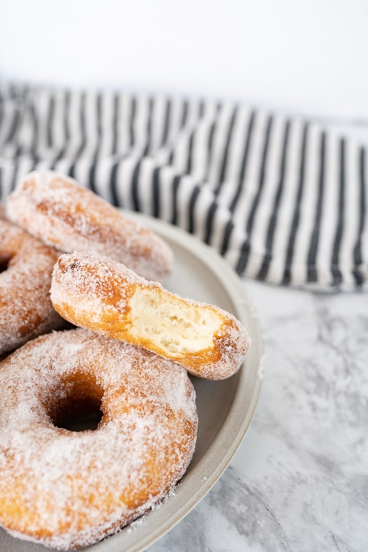 A bowl with sugar donuts sitting on the counter. Next to the bowl is a black and white striped towel. The top donut in the bowl has a bite taken out of it. 