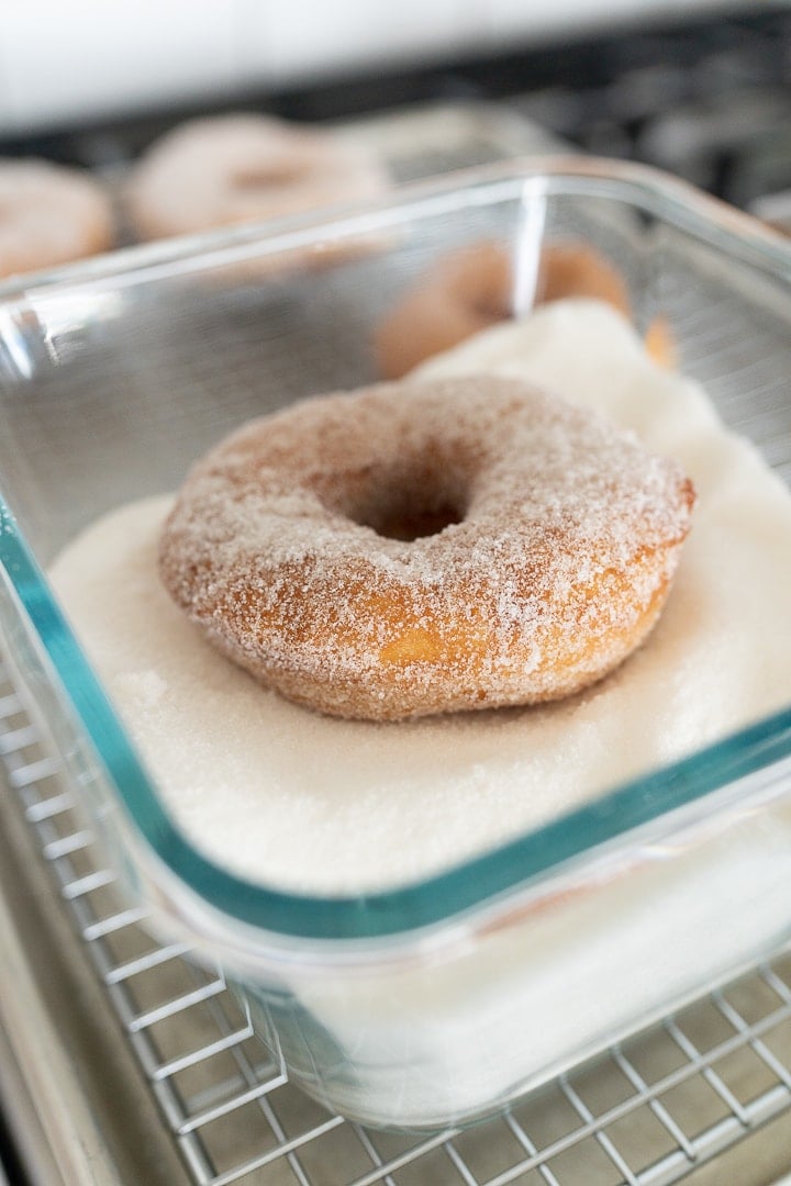 A pan of granulated sugar with a donut sitting in it. 