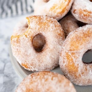 A pile of fried donuts sitting on the counter next to a gray and white striped towel. One of the sugar donuts has a bite out of it.