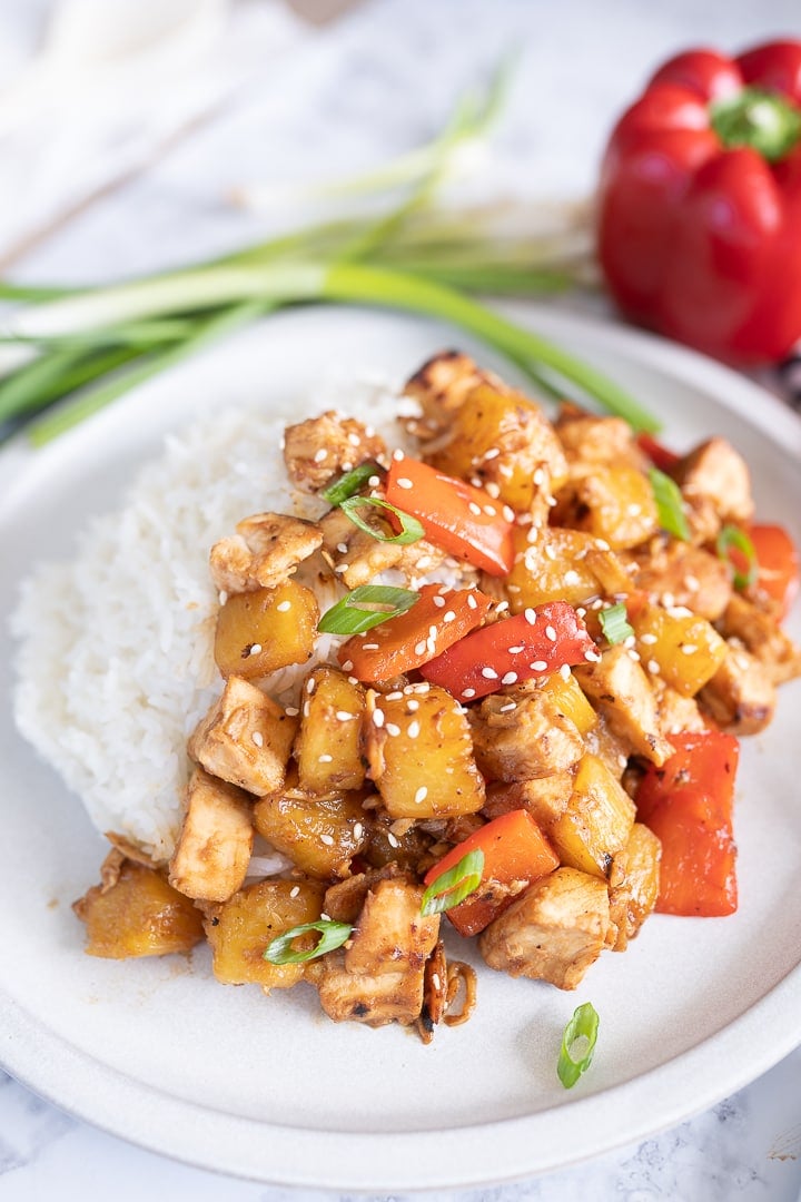 Hawaiian chicken with pineapple and red bell peppers covers rice on a plate. 