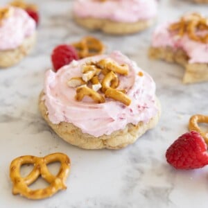 Raspberry pretzel cookies sit on a counter. In the background you can see additional cookies and raspberries and pretzels scattered around.