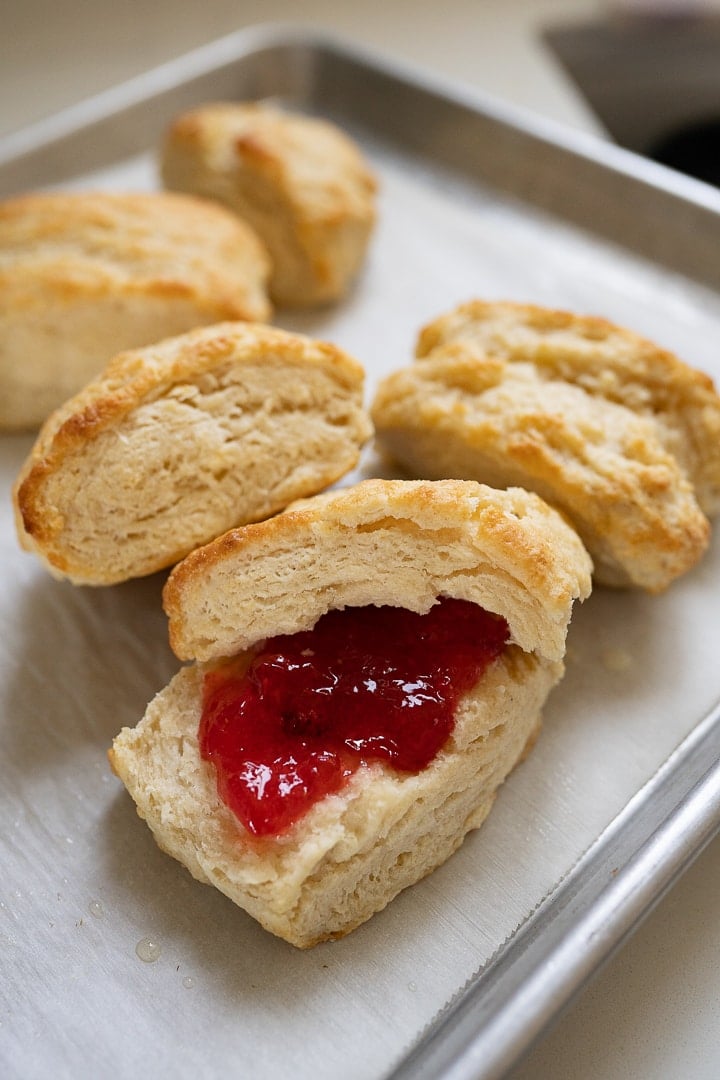 Buttermilk biscuits on a plate. One has been cut open and topped with jam. 