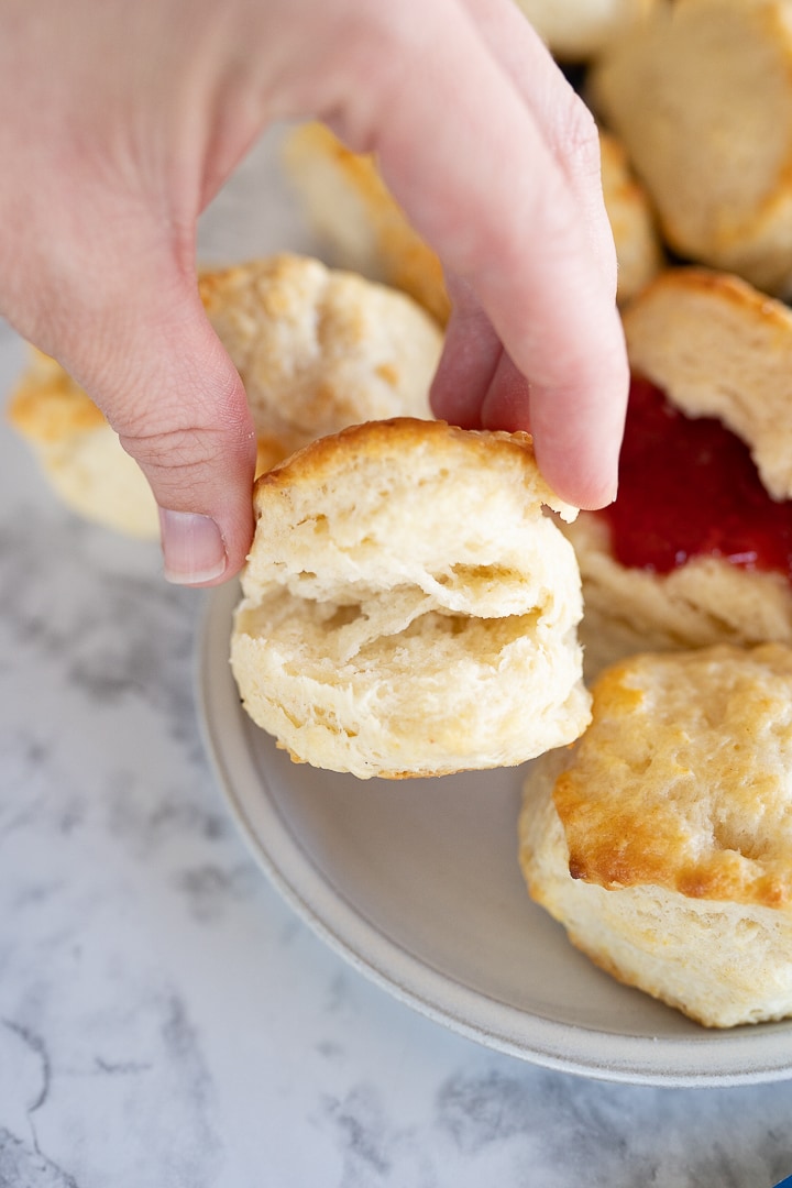 A hand holding a buttermilk biscuit, pinching the sides to show the flaky layers. 