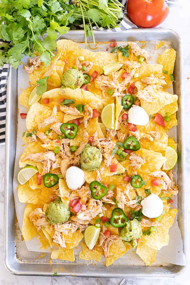 Aerial view of chicken nachos on a sheet pan with all the toppings. 