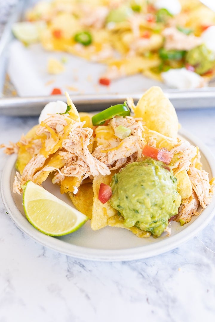 Chicken nachos plated on a white dish with guacamole and a lime slice. 