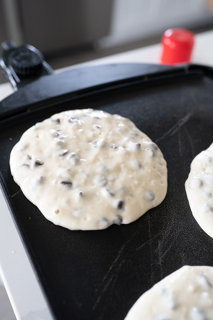 Chocolate chip pancakes being cooked on a griddle. 