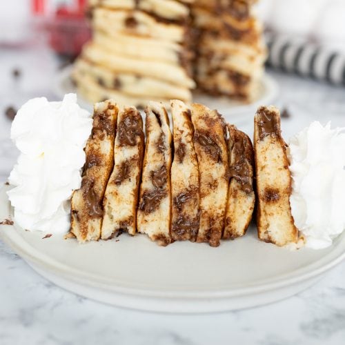 Side view of a stack of chocolate chip pancakes, cut and on its side. Topped with whipped cream.
