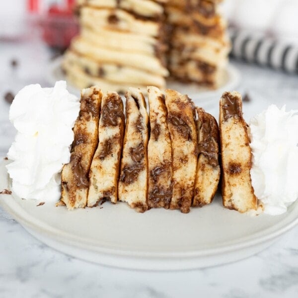 Side view of a stack of chocolate chip pancakes, cut and on its side. Topped with whipped cream.