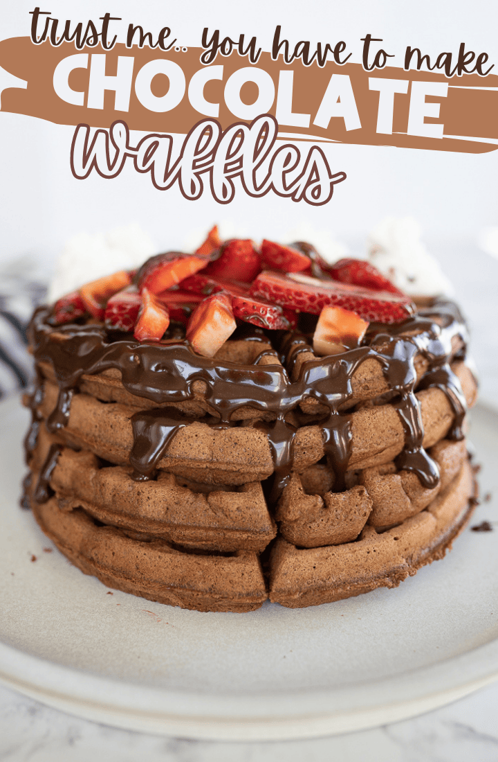 Chocolate waffles stacked high on a plate. Topped with chocolate syrup and cut up strawberries. Across the top it says "trust me, you have to make chocolate waffles"