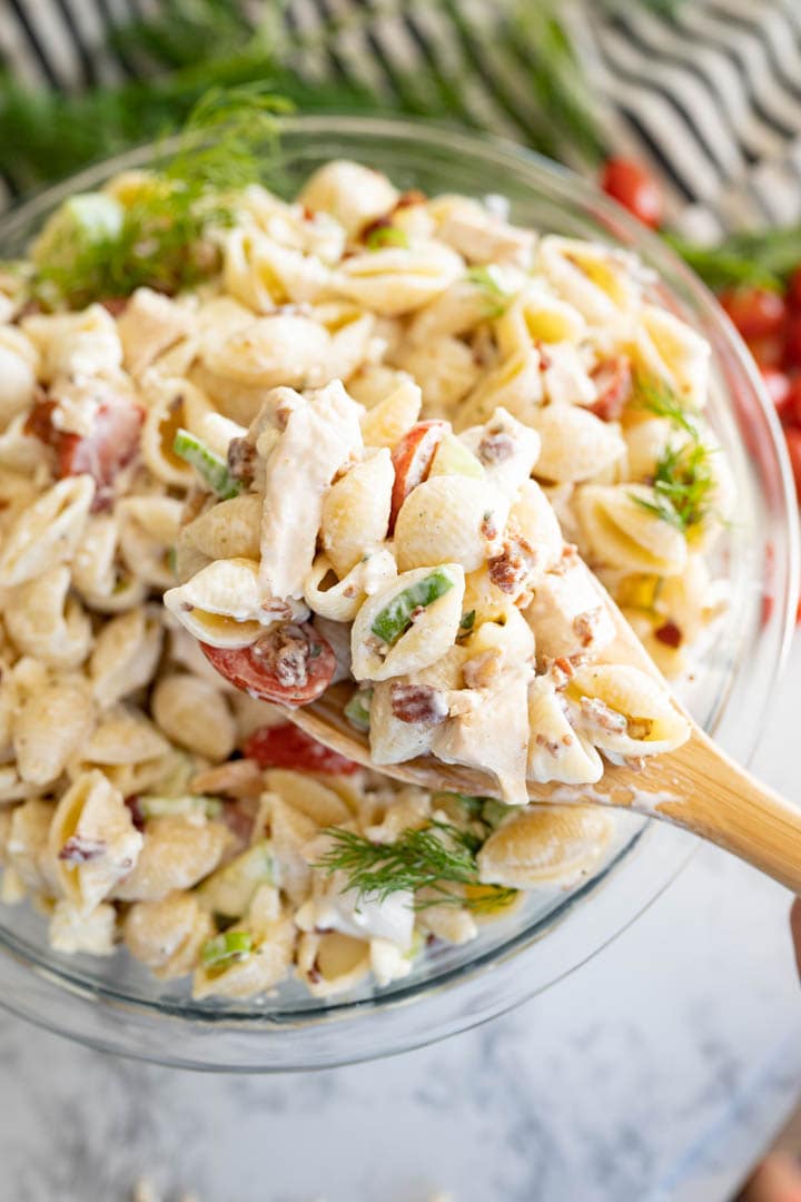 Bowl of chicken bacon ranch pasta salad with a wooden spoon scooping a serving out. 