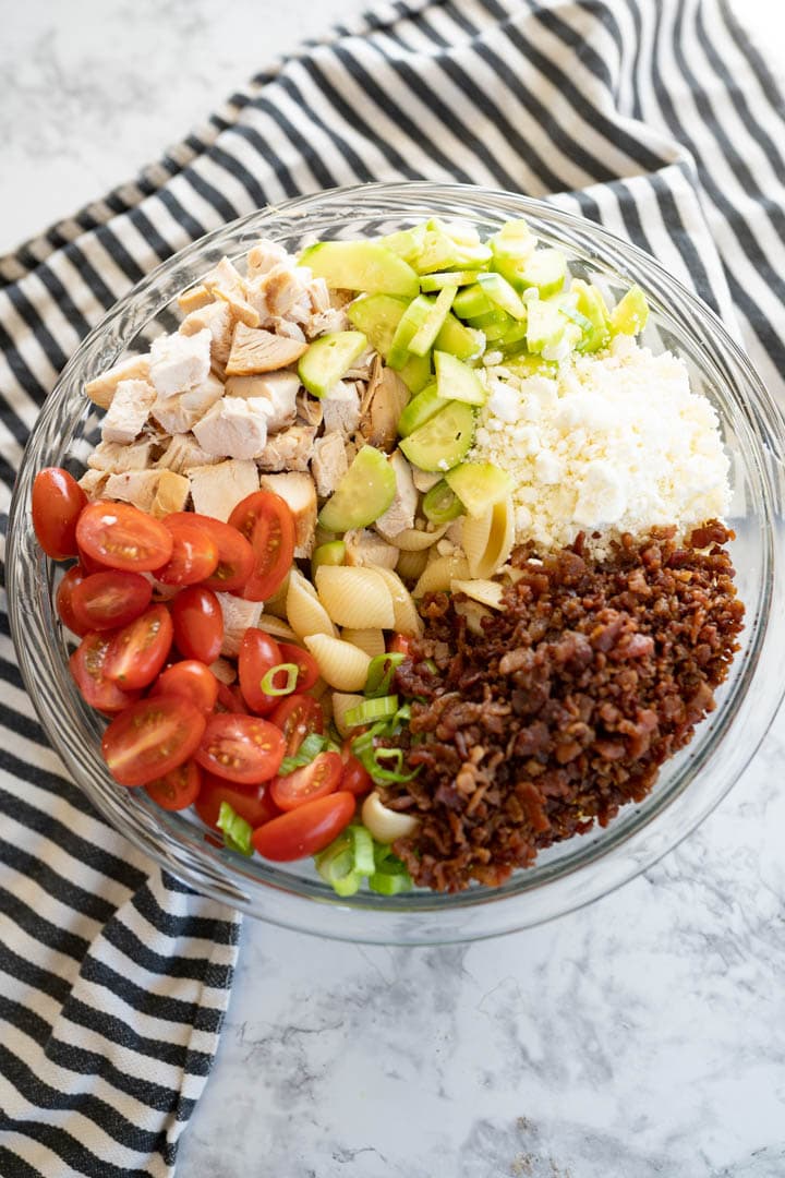 A bowl with all of the ingredients for chicken pasta salad arranged separately prior to being mixed up. 