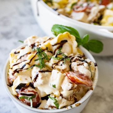 A bowl of chicken caprese pasta next to a serving dish.