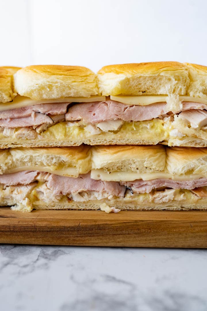 Side view of 6 chicken cordon bleu sliders stacked on top of each other on a wooden cutting board. 