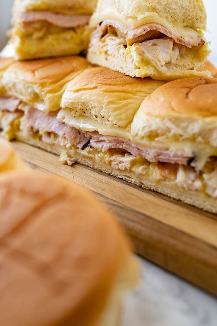 Side view of chicken cordon bleu sliders stacked on each other on a wooden cutting board. 
