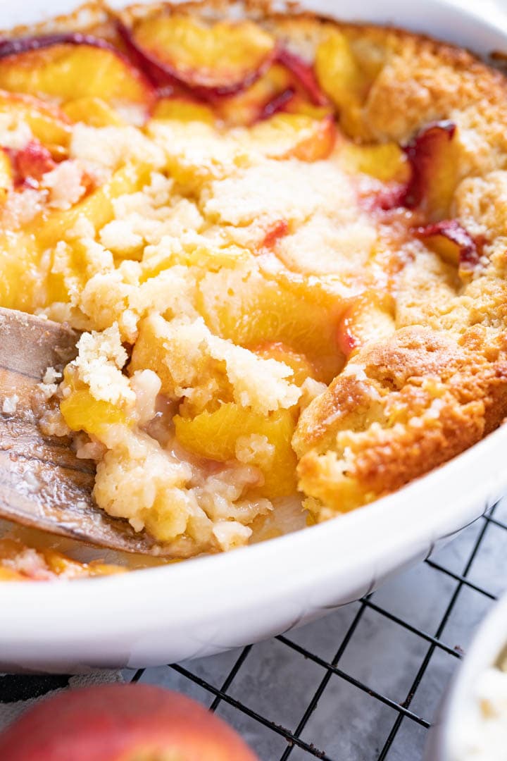 A spatula scooping peach cobbler out of the pan. 