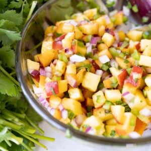 Serving bowl of peach salsa. On the counter next to it is a bunch of cilantro.
