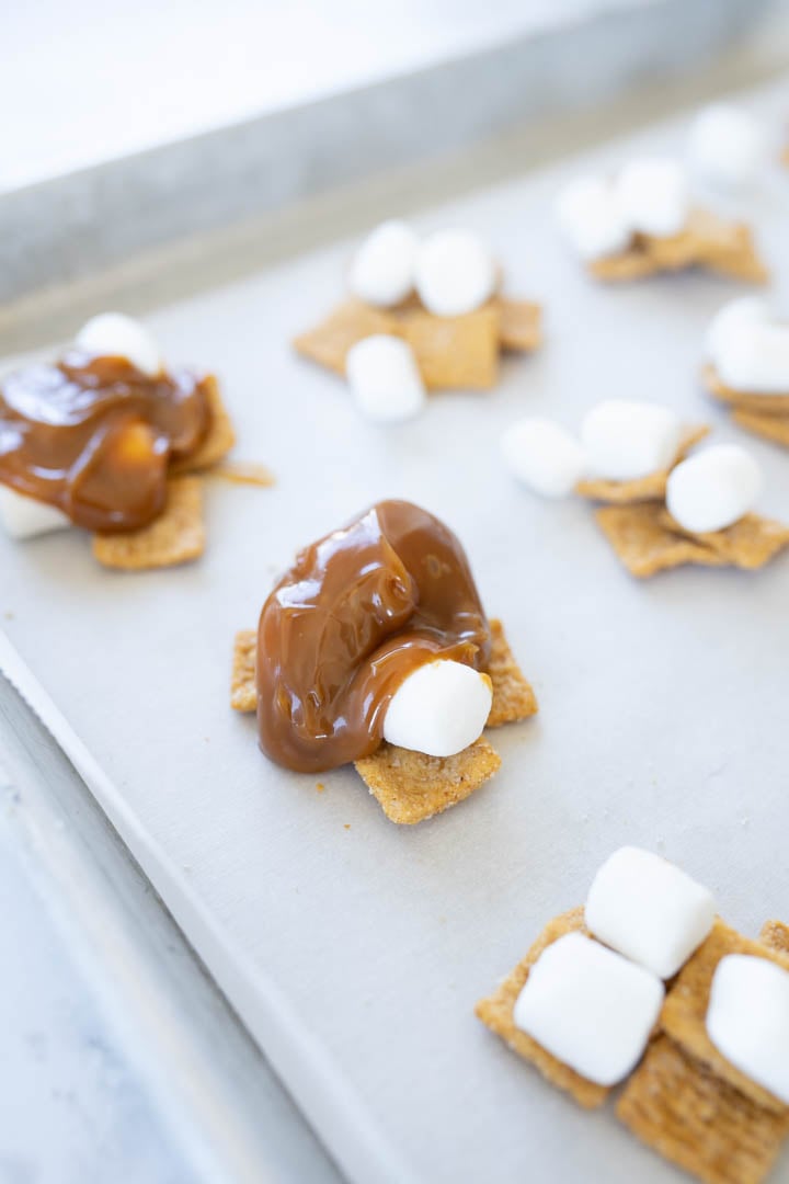 Golden grahams + marshmallows topped with caramel dip in the process of making costco caramel s'mores clusters. 