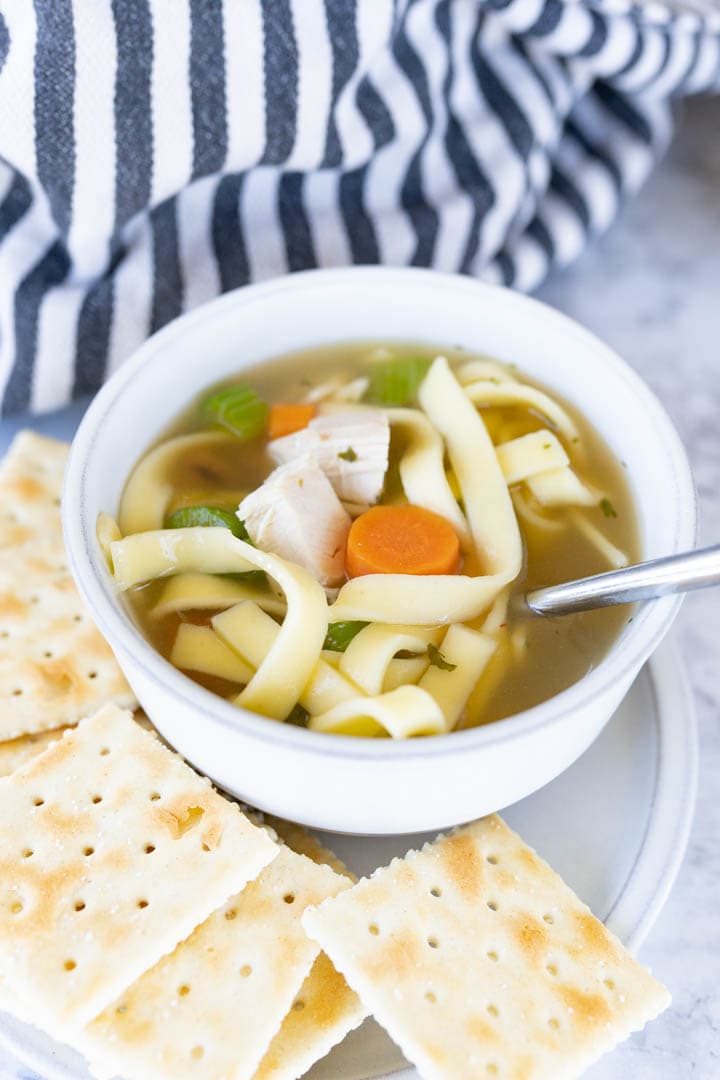 A single serving bowl of homemade chicken noodle soup served with crackers. 