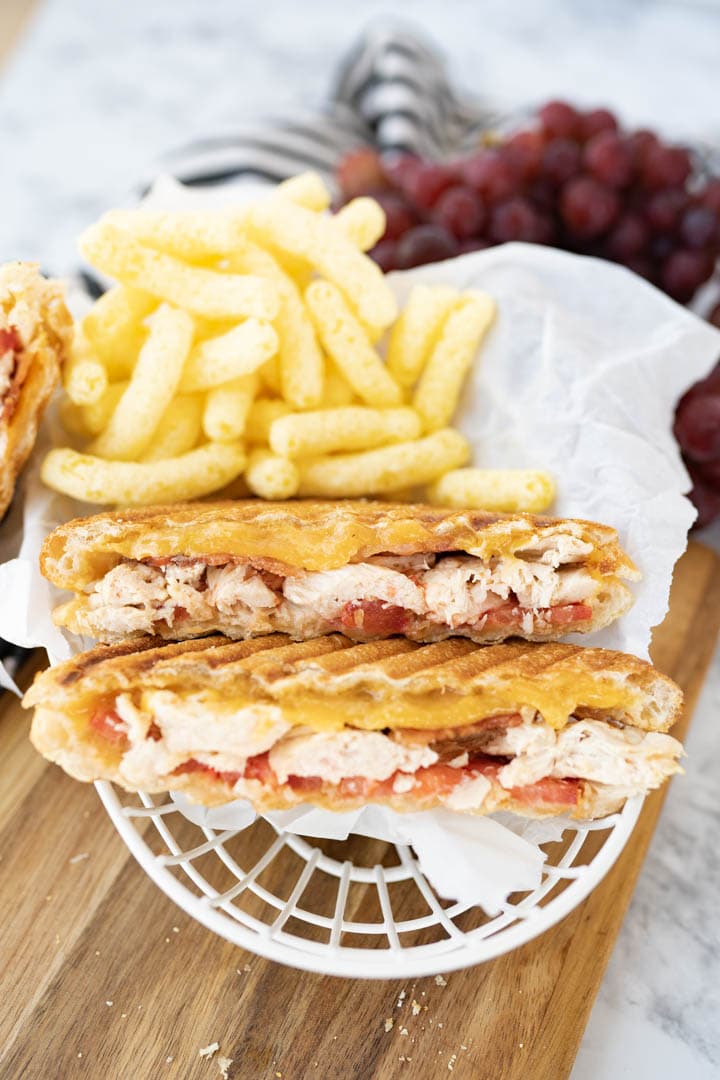 A grilled chicken panini cut in half and plated with puffed chips and grapes. 