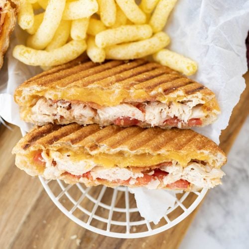 A grilled chicken panini cut in half and plated with puffed chips.