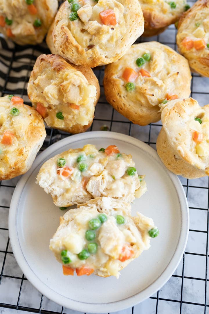 A pile of mini chicken pot pies next to a serving plate with a pot pie split open. 